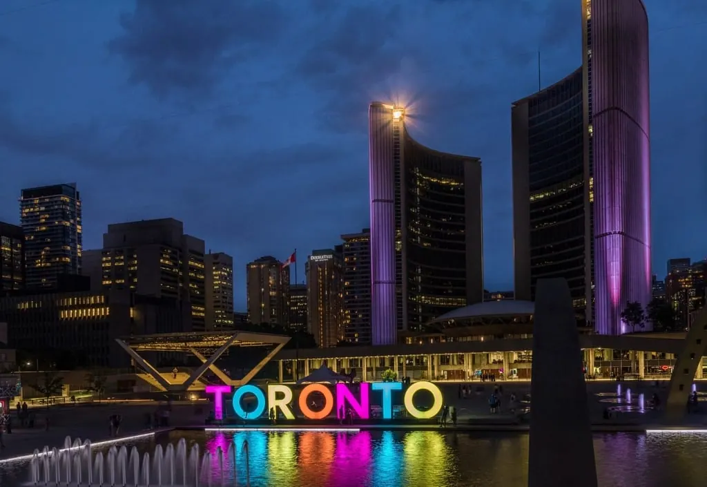 해질 무렵 토론토 시청 앞 광장에 설치된 색색의 TORONTO 조형물과 분수, 뒤편의 곡선형 시청 건물