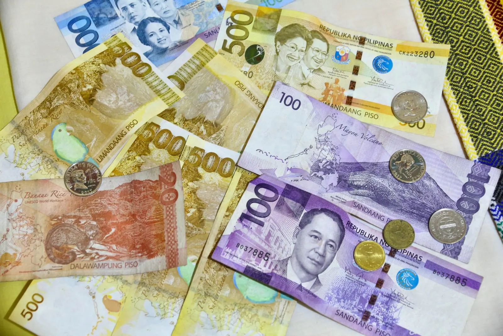 Philippine peso banknotes and coins spread out on a patterned cloth — 20, 100, 500 and 1,000 peso notes