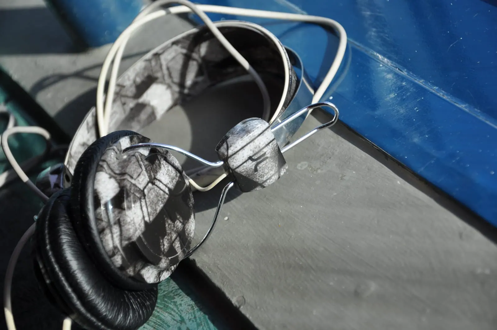 Unos auriculares sobre un banco iluminado por el sol: diadema de alambre cromado, almohadillas con estampado en blanco y negro y un cable blanco enredado