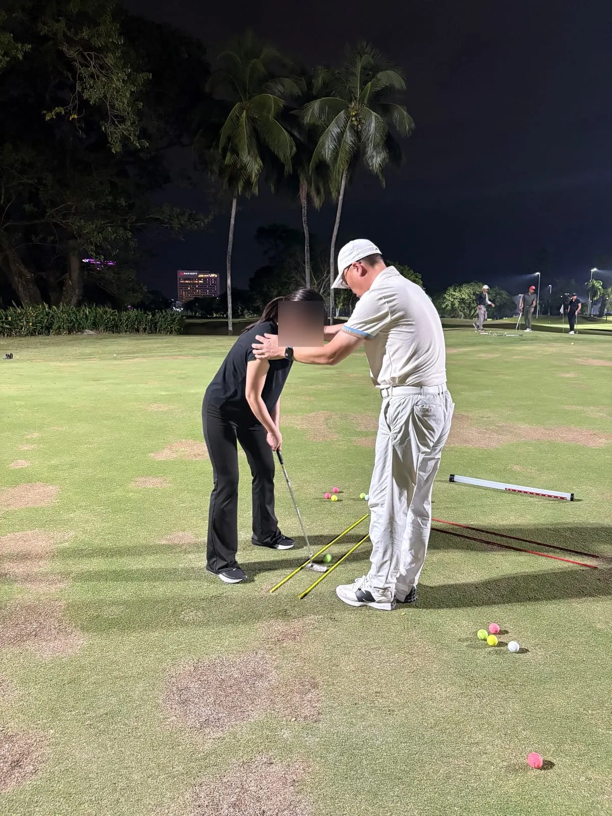 Teaching pro correcting a student’s putting posture on the green at night