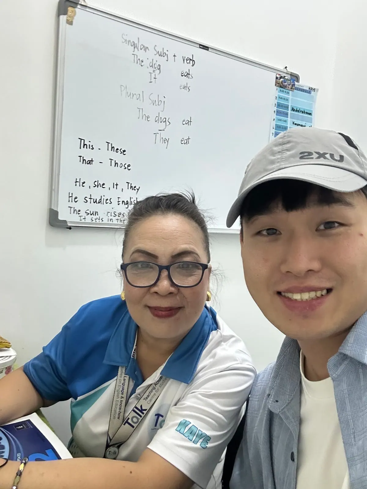 학생과 선생님이 함께 찍은 사진, 뒤 화이트보드에 기초 문법이 적혀 있다