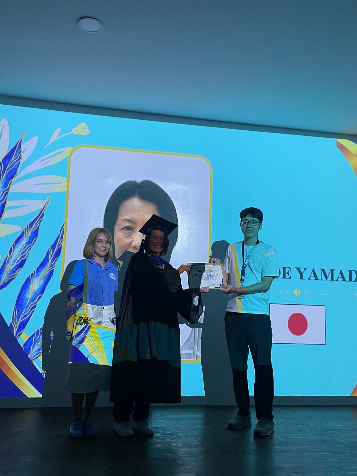 Receiving a certificate on the graduation stage, with the Japanese flag displayed on the screen behind