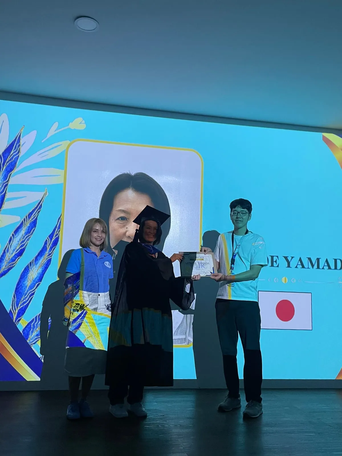 Receiving a certificate on the graduation stage, with the Japanese flag displayed on the screen behind