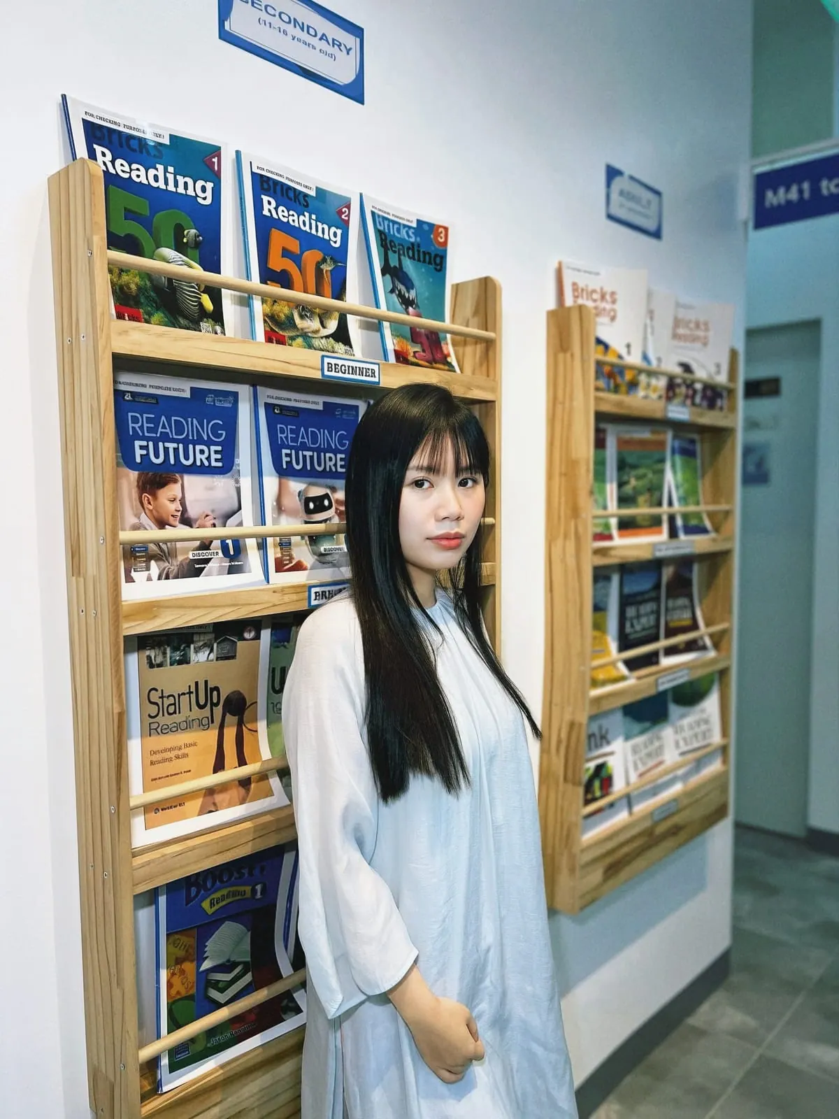 Ngoc Thao ao lado das prateleiras de livros didáticos da escola