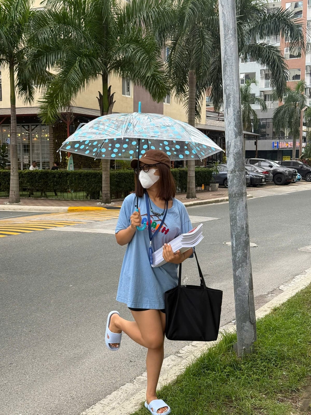 Van Anh walking along a street in Clark with an armful of coursebooks and an umbrella